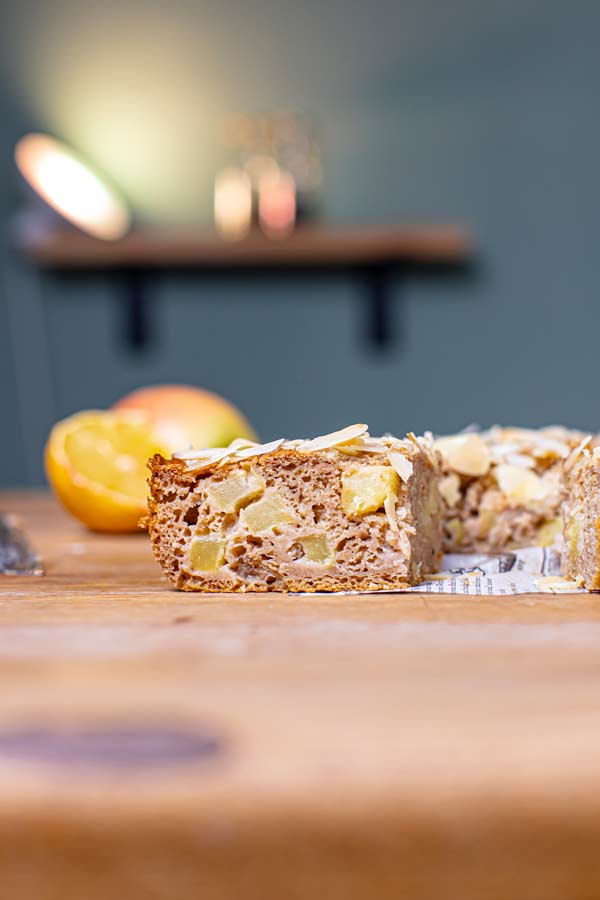 ein stueck veganer apfelkuchen von vorne auf einem holztisch mit deko im hintergrund