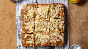 veganer apfelkuchen von oben mit mandeln garniert und in gleichgroße stuecke geschnitten