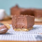 Nahaufnahme einer Scheibe Schokoladen-Käsekuchen mit krümeligem Boden und strukturierter Oberfläche auf einem bedruckten Papier.