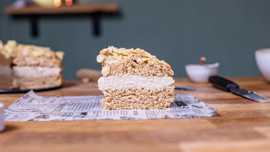 ein stueck veganer bienenstich von vorne auf einem weissen backpapier auf einem holztisch mit dekoration