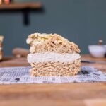 ein stueck veganer bienenstich von vorne auf einem weissen backpapier auf einem holztisch mit dekoration