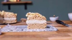 ein stueck veganer bienenstich von vorne auf einem weissen backpapier auf einem holztisch mit dekoration