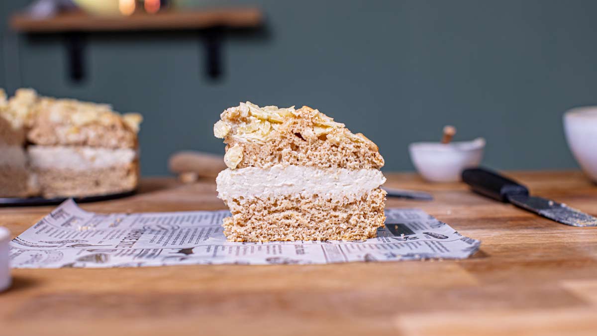 ein stueck veganer bienenstich von vorne auf einem weissen backpapier auf einem holztisch mit dekoration