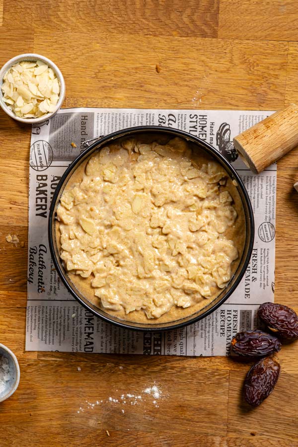 bienenstich teig mit mandeltopping in einer schwarzen springform von oben auf holztisch mit deko
