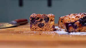 blaubeerkuchen stueck von vorne auf holztisch mit sichtbarer porung und blaubeeren