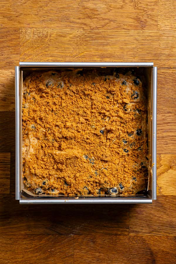 teig fuer blaubeerkuchen in einer kastenform von oben mit streuseln bedeckt auf holztisch