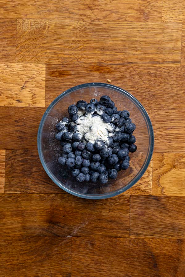 blaubeeren und etwas mehl in einer glasschuessel von oben auf einem holztisch