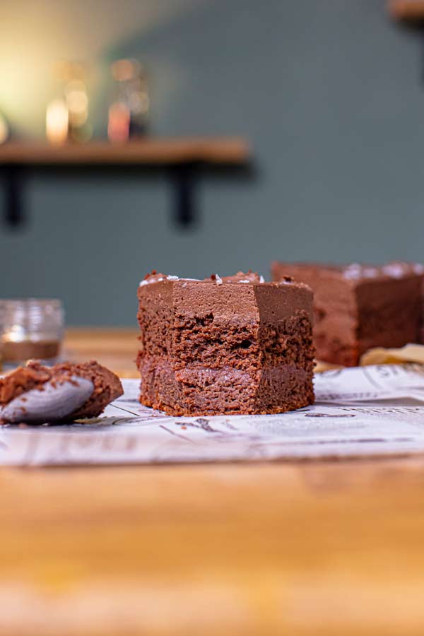 stueck vegane schokotorte von vorne mit einem loeffel und der gesamten torte im hintergrund