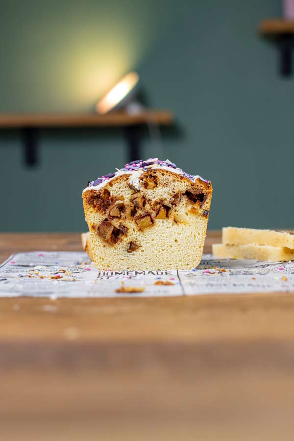 fertig gebackener ruehrkuchen mit apfel von vorne angeschnitten auf einer holzplatte