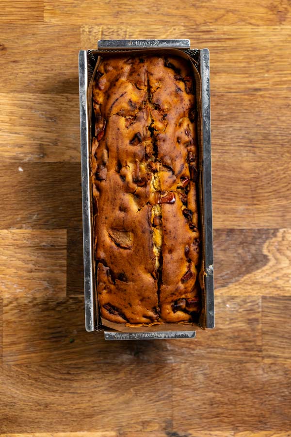 gebackener ruehrkuchen mit apfel in einer backform von oben auf einer holzplatte
