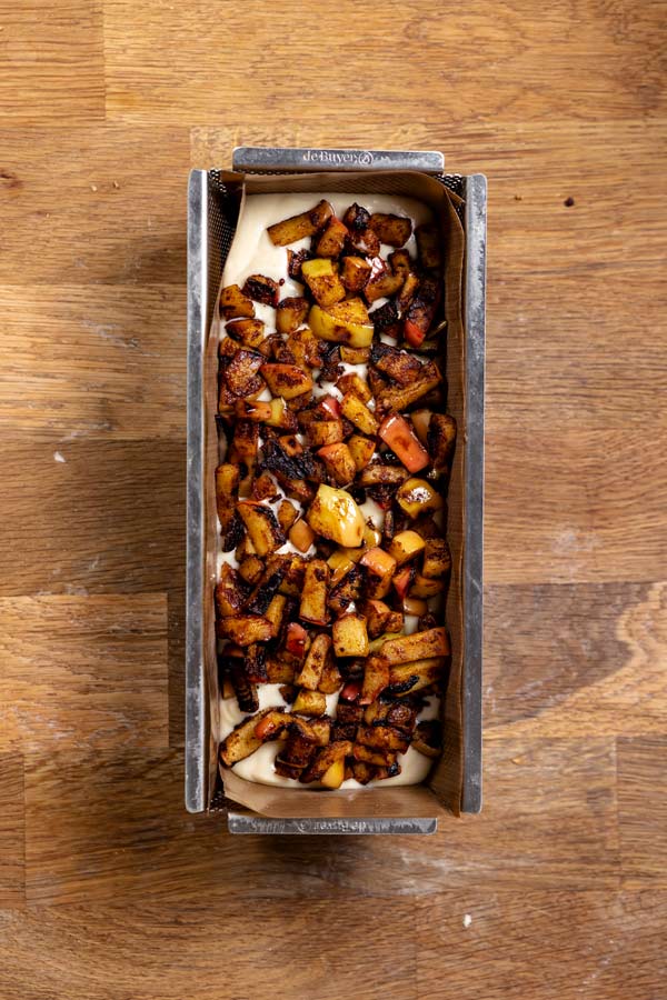 apfel topping mit gebratenen aepfeln auf dem rohen teig in einer kastenform von oben auf einer holzplatte