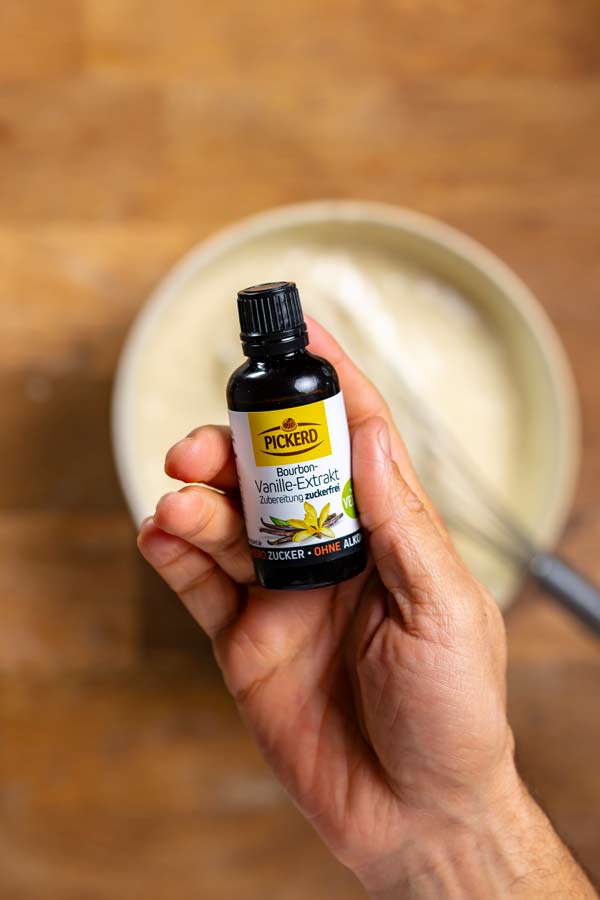 vanilleextrakt flasche in einer hand von oben ueber einer schuessel auf einem holztisch