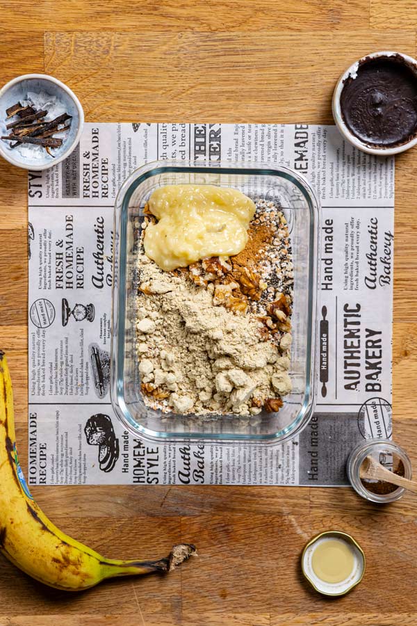 trockene zutaten mit proteinpulver fuer buchweizen porridge in einem glascontainer von oben auf einem holztisch mit weissem backpapier