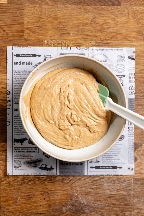 fertig vermengter teig fuer blaubeer streusel kuchen in einer schuessel mit spatula von oben auf holztisch
