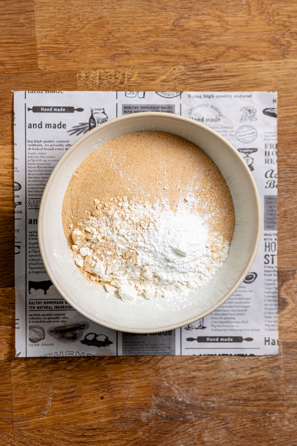 trockene und feuchte zutaten fuer blaubeer streusel kuchen in einer weissen schuessel von oben auf einem weissen backpapier auf einem holztisch