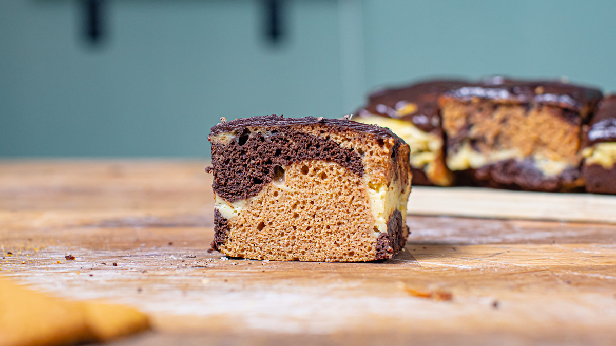 ein stueck gesunder marmorkuchen von vorne auf einem holztisch mit uebrigem kuchen im hintergrund