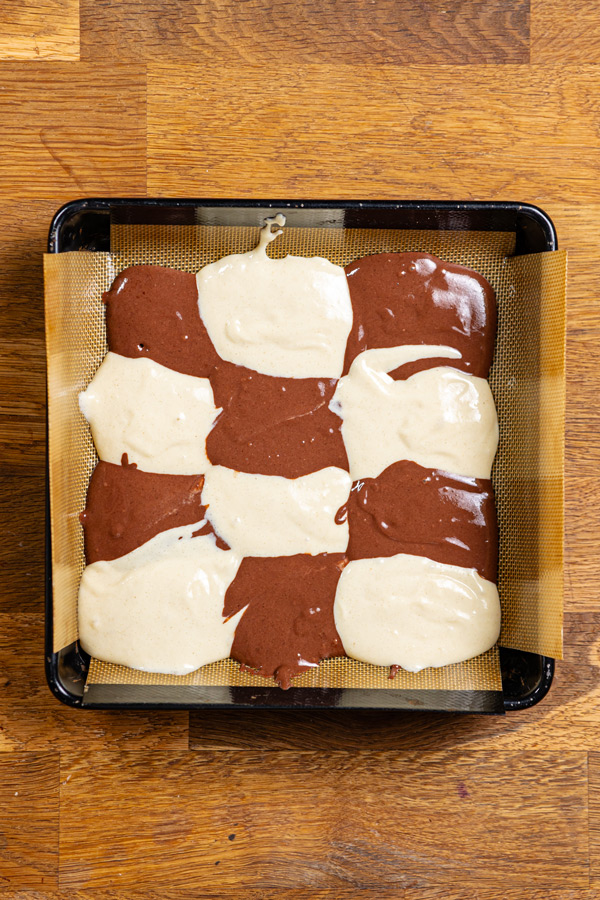 erste schicht heller und dunkler teig fuer donauwellen kuchen in einer quadratischen backform von oben auf holztisch