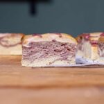 ein stueck veganer erdbeerkuchen mit weiteren stuecken im hintergrund auf einem holztisch