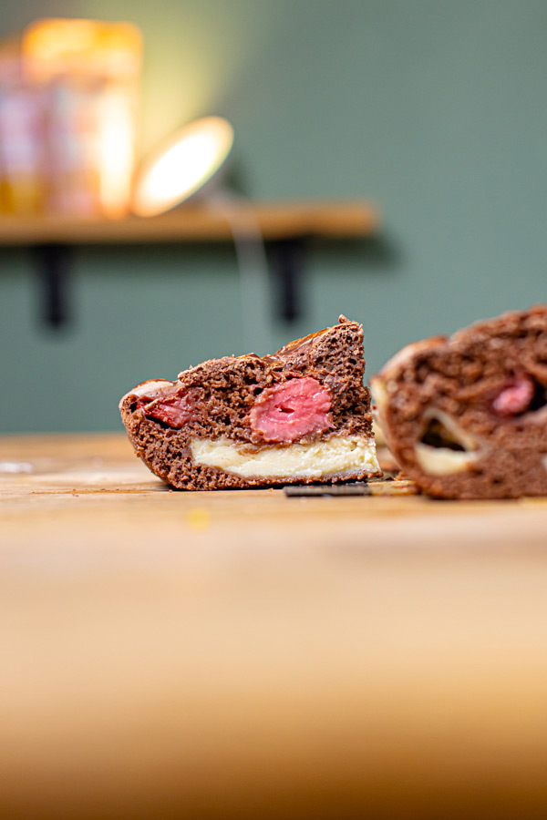 nahaufnahme frontal von einem stueck erdbeer schokokuchen mit cheesecake fuellung auf einem holztisch mit blau gruenem hintergrund