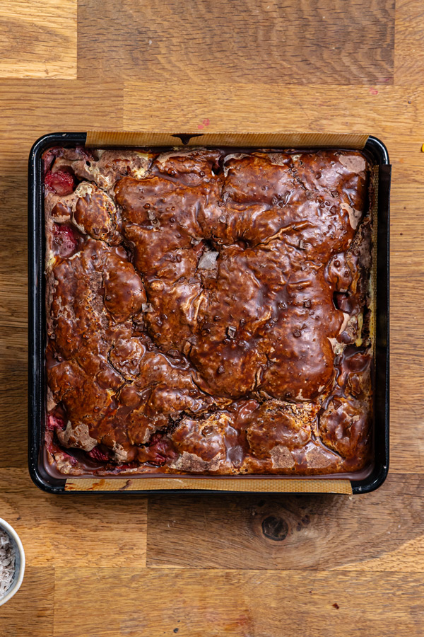 fertiger erdbeer schokokuchen von oben in einer schwarzen viereckigen backform auf einem holztisch