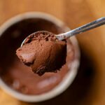 schokoganache auf einem kleinen loeffel von oben über einer schuessel auf einem holztisch