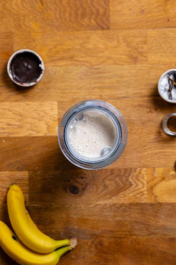 bananenmilch gemixt aus reifer banane und milch in einem mixbehaelter von oben auf einem holztisch mit deko