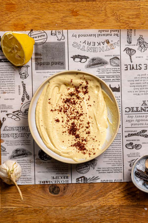 fertiger hummus von oben in einem runden teller auf weissem backpapier mit essigbaumgewuerz garniert