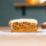 stueck karottenkuchen mit frosting frontal auf einem holztisch