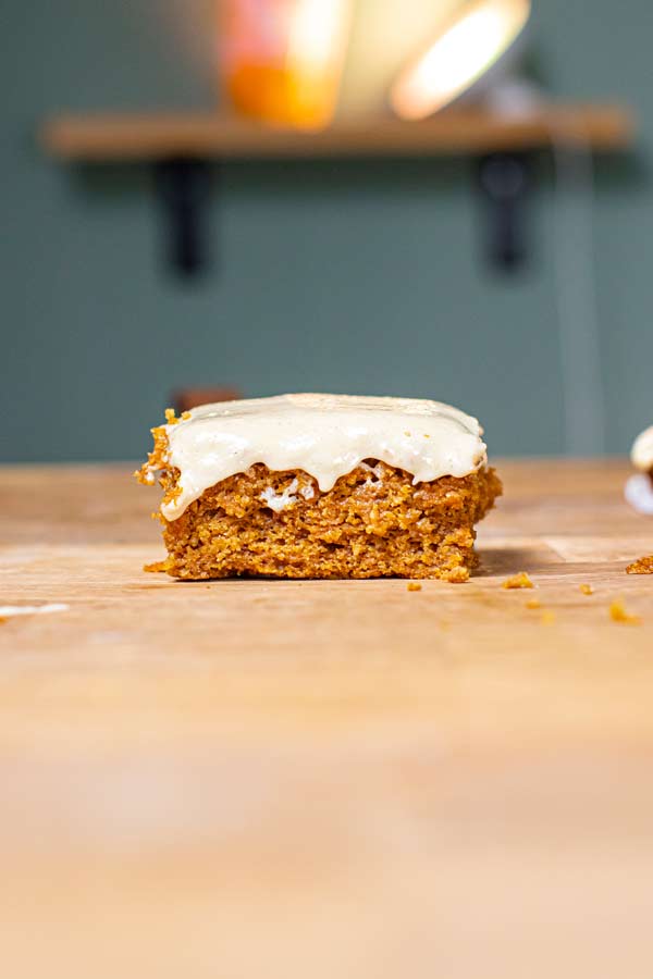 ein stueck karottenkuchen mit frosting auf einem holztisch frontal aufgenommen