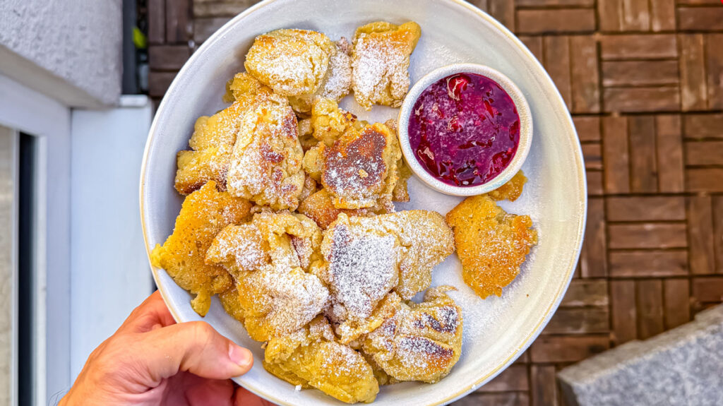 teller veganer kaiserschmarrn mit roter gruetze von oben auf einem runden teller mit holzbelag im hintergrund