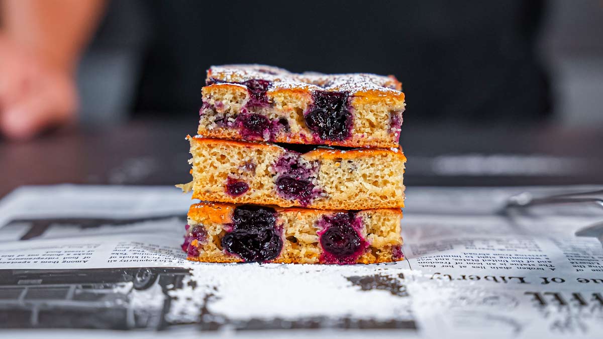 drei stuecke kirschkuchen vom blech aufeinander gestapelt von vorne auf weissem backpapier