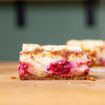 stueck kirsch kaesekuchen von vorne frontal auf einem holztisch mit anderen stuecken im hintergrund