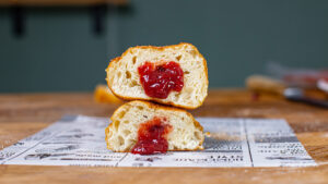 zwei aufeinander berliner krapfen haelften auf einem tisch von vorne mit sichtbarer marmeladenfuellung