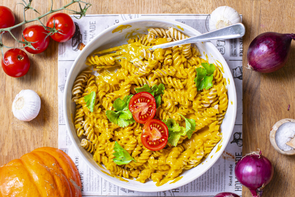 kuerbis mac and cheese in rundem teller garniert mit tomate und basilikum auf tisch mit deko