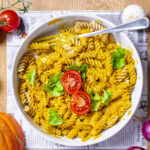 kuerbis mac and cheese in rundem teller garniert mit tomate und basilikum auf tisch mit deko
