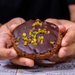 veganer lebkuchen wird in zwei haenden gehalten von vorne mit pistazien garniert