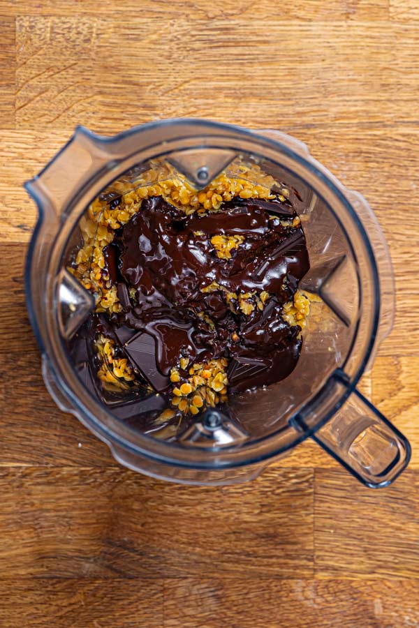 linsen und darüber geschmolzene schokoladenstuecke in einem mixbehaelter von oben auf einem holztisch