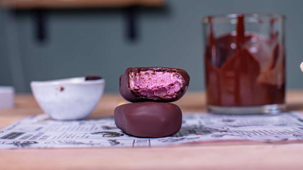 zwei gesunde magnum eis aufeinander gestapelt mit sichtbarer rosa fuellung von vorne auf holztisch mit deko