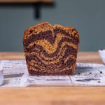 veganer marmorkuchen angeschnitten mit gut erkennbarem muster von vorne auf einem bedruckten backpapier mit deko