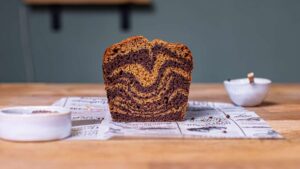 veganer marmorkuchen angeschnitten mit gut erkennbarem muster von vorne auf einem bedruckten backpapier mit deko