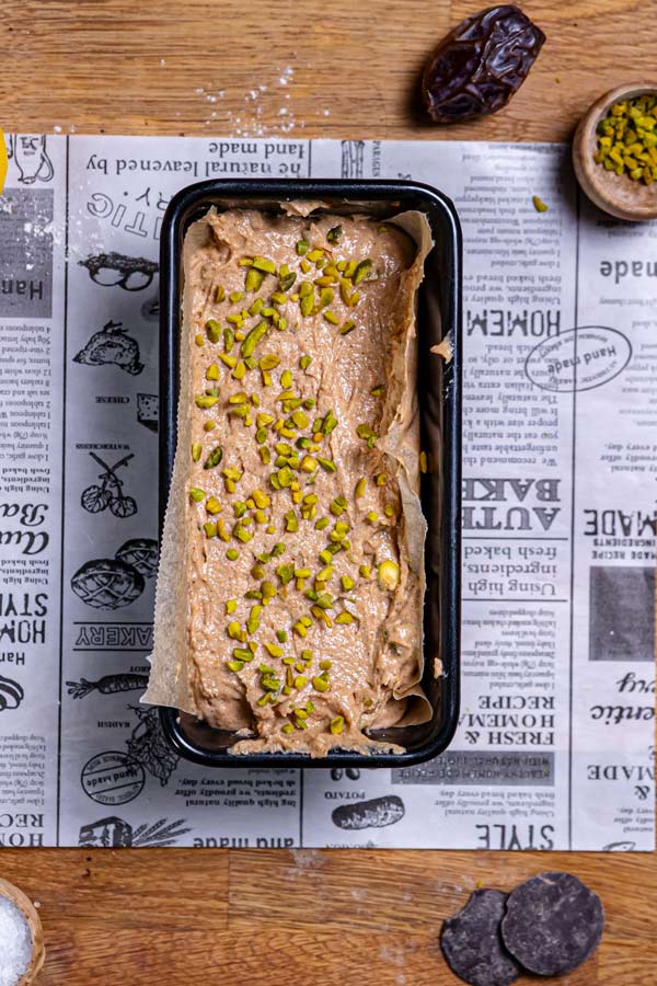 teig fuer kuchen mit pistazien in kastenform mit pistazien dekoriert von oben auf holztisch