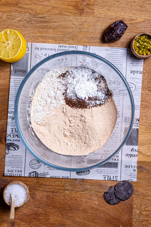 trockene zutaten fuer kuchen mit pistazien in glas schuessel von oben auf holztisch mit deko