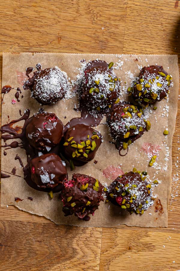 fertige pralinen mit schokolade von oben auf einem backpapier mit verschiedenen nuessen garniert