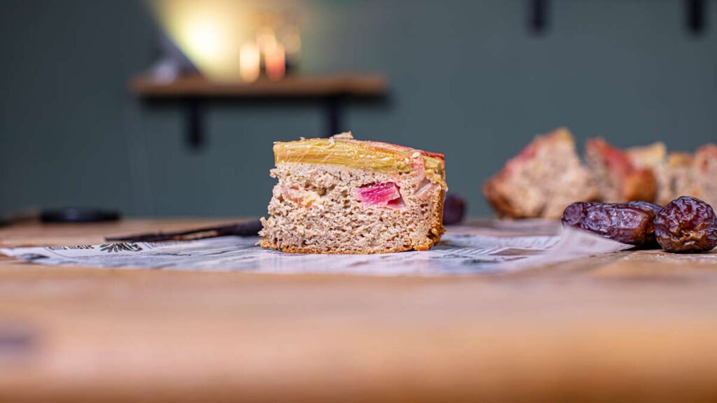 ein stueck veganer rhababerkuchen auf einem holztisch von vorne mit unscharfem hintergrund