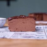 stueck vegane schokotarte von der seite auf einem weissen backpapier auf einem holztisch