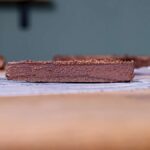 ein stueck schokotart von der seite auf einem holztisch mit weissem backpapier