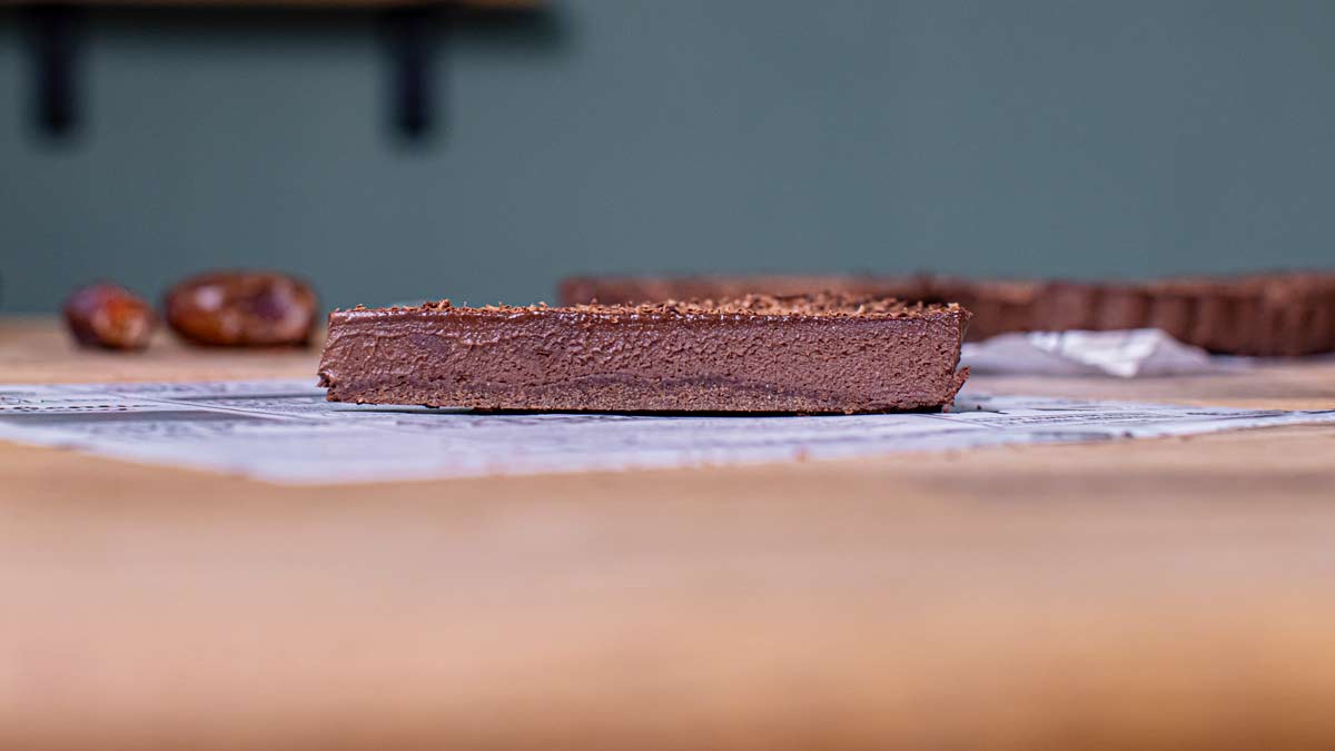 ein stueck schokotart von der seite auf einem holztisch mit weissem backpapier