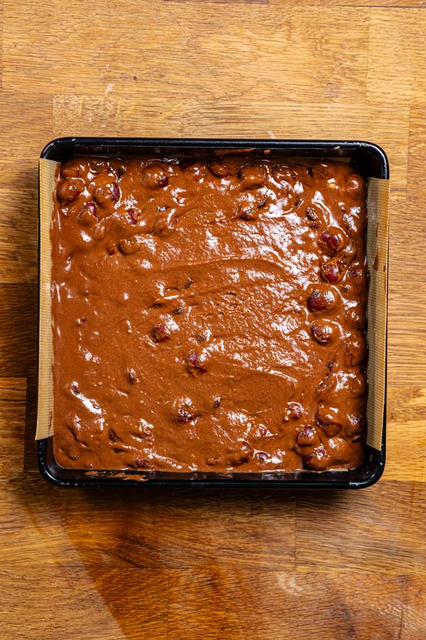roher teig fuer schwarzwaelder kirsch kuchen in schwarzer quadratischer backform von oben auf holztisch