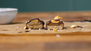 selbstgemachtes gesundes snickers halbiert mit beiden haelften nebeneinander auf einem holzbrett von vorne