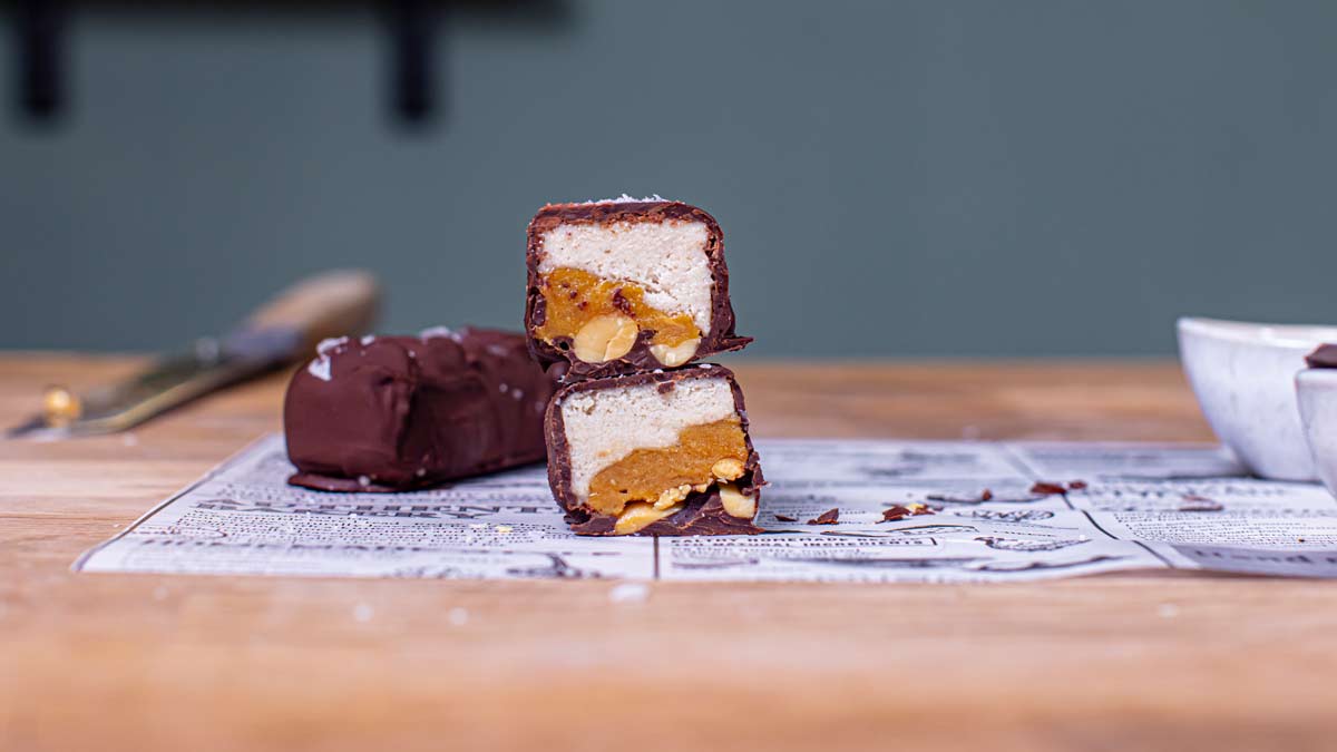 snickers eis halbiert und aufeinander gestapelt von vorne auf einem holztisch auf weissem backpapier